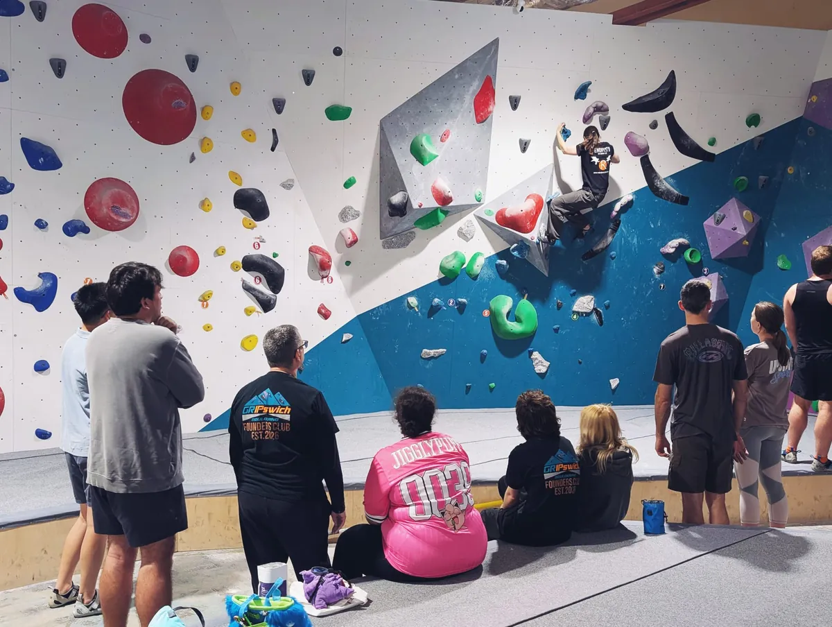 A climber reaching for a hold on the overhanging volumes at GRIPswich while the rest of the Bouldering 101 class watches from the mats